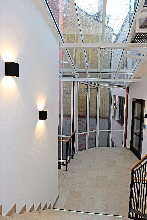 Lichtdurchflutet präsentiert sich das Treppenhaus als Verbindungstrakt der einzelnen Gebäudeteile. Im Lichthof ist ein in Rot gehaltenes Kunstwerk platziert, das in Zusammenarbeit mit den Ruperti Werkstätten in Altötting entstanden ist. − Foto: Brunner