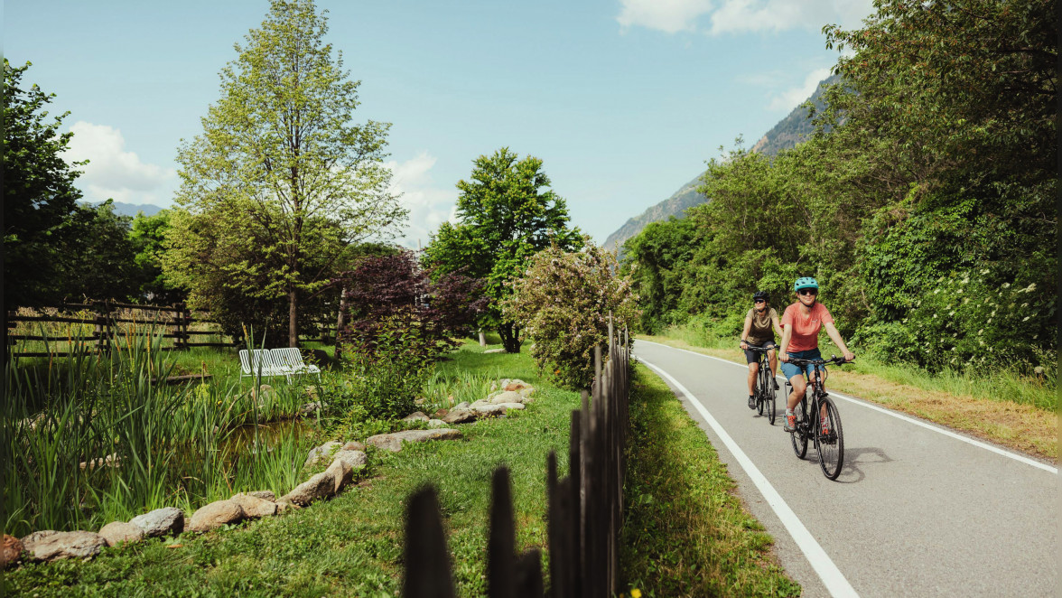 Biken auf dem Etschradweg entlang frühlingsblühender Bäume. Links im Bild lockt der Teich an der NATURnser Radbar zur Rast. Foto: IDM Südtirol/Alex Moling